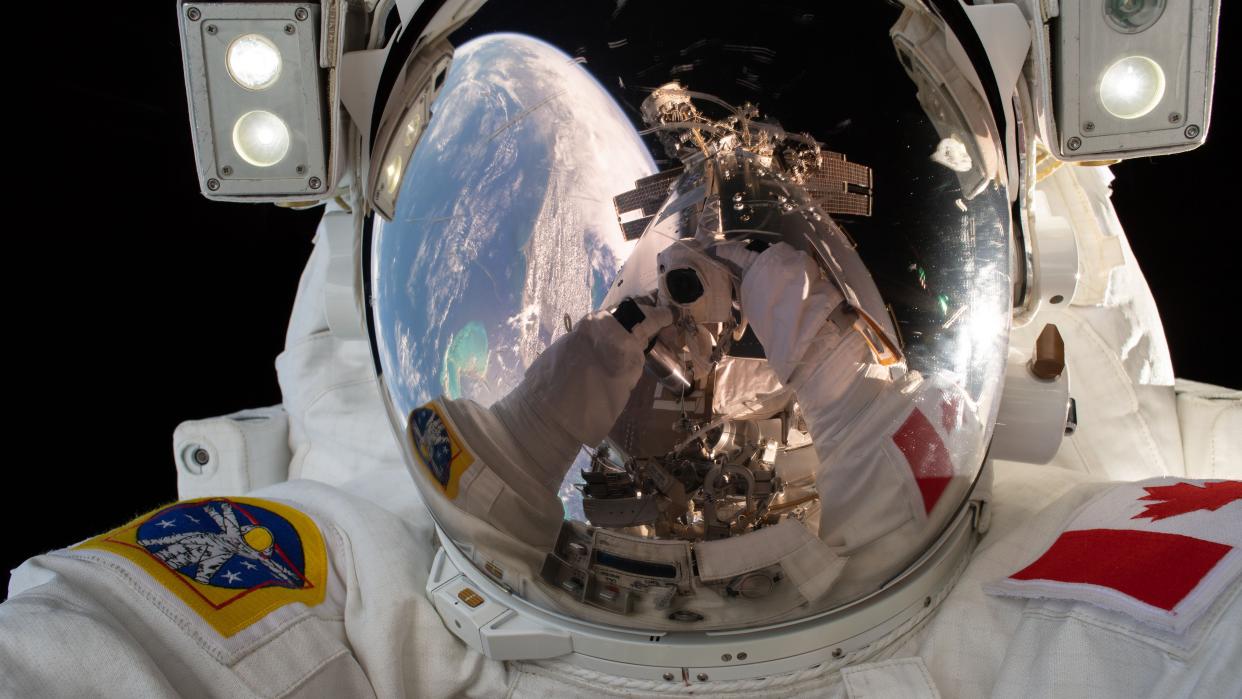  An astronaut in a spacesuit. you can see his gloved hands taking a picture in the reflection from his helmet. also in the reflection is earth and a strut of the international space station. 