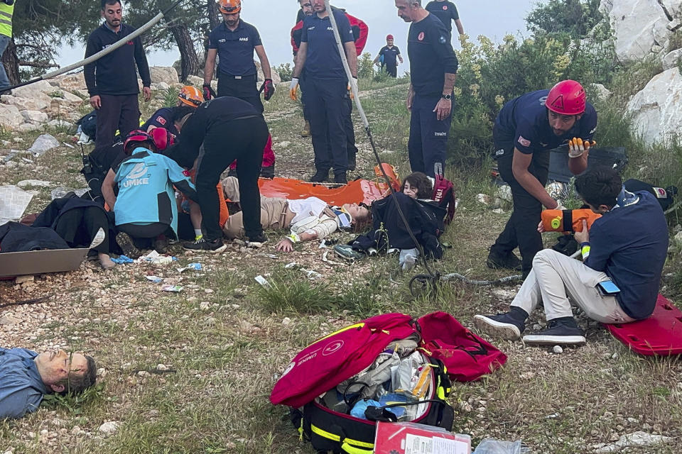 Rescue and emergency team members work with passengers of a cable car transportation system outside Antalya, southern Turkey, Friday, April 12, 2024. At least one person was killed and several injured Friday when a cable car pod in southern Turkey hit a pole and burst open, sending the passengers plummeting to the mountainside below, officials and local media said. Scores of other people were left stranded late into the night after the entire cable car system came to a standstill. (Dia Images via AP)