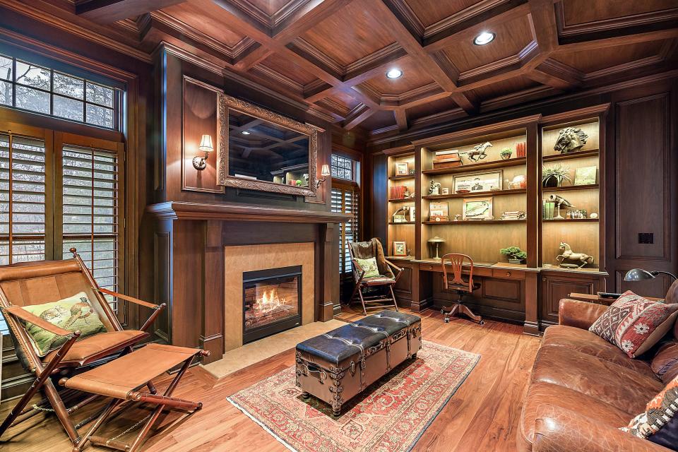 An office with custom walnut paneling, coffered ceiling, a gas fireplace with leathered granite surround and a Séura framed TV on the first level.