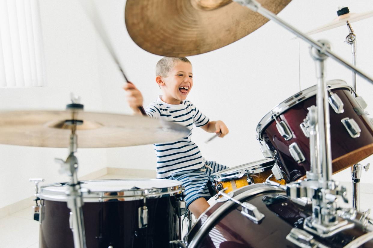 Smiling little boy wildly playing a 4-piece drum set having fun with a white wall in the background