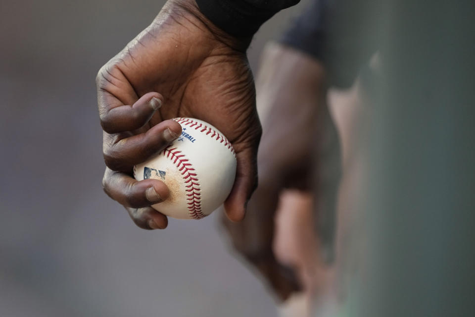 A New York Yankees player holds a baseball as he watches from the dugout during the team's game against the Atlanta Braves, Wednesday, Aug. 16, 2023, in Atlanta. (AP Photo/John Bazemore)