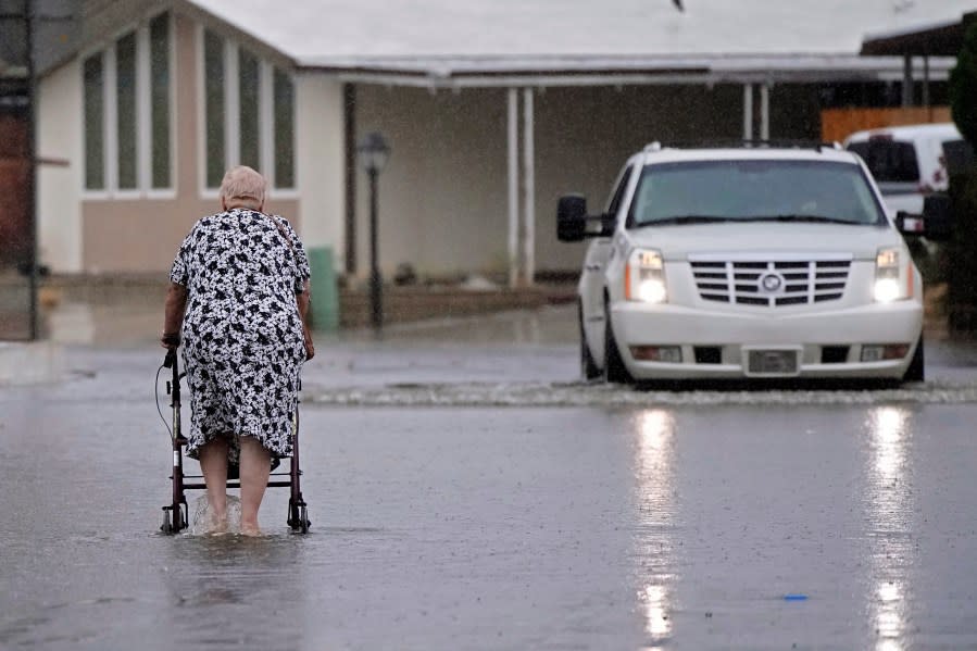 An elderly woman crosses a street flooded by torrential rain brought by Tropical Storm Hilary, Sunday, Aug. 20, 2023, in Thousand Palms, Calif. (AP Photo/Mark J. Terrill)