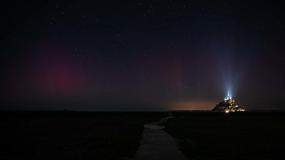 France's iconic medieval abbey Mont-Saint-Michel with a glow of aurora borealis in the background.