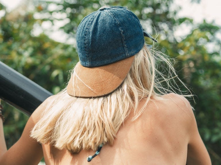 woman sitting looking at trees wearing a bathing suit and a backwards baseball hat