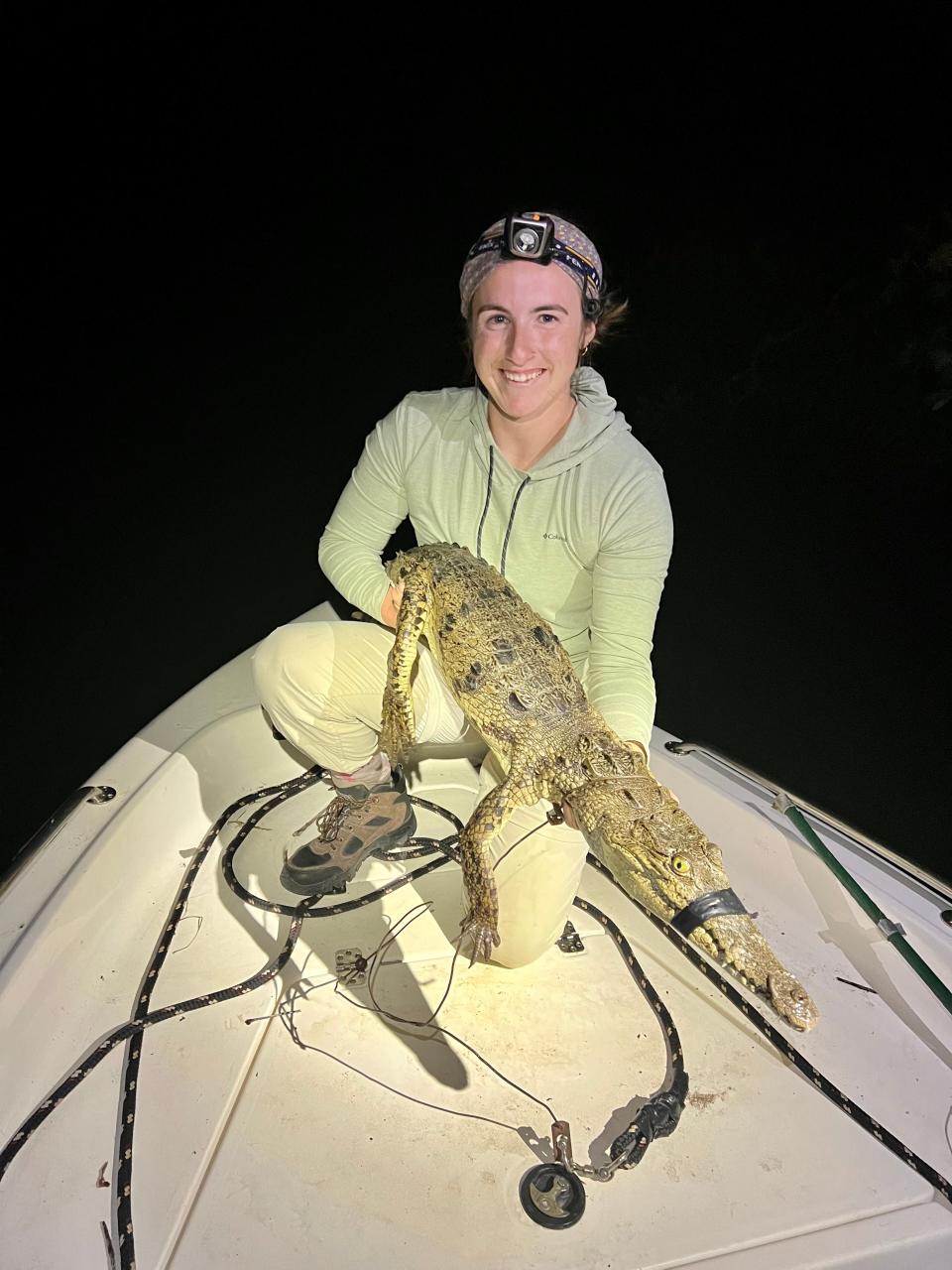 A woman on a boat holding a medium-sized crocodile with its mouth taped.