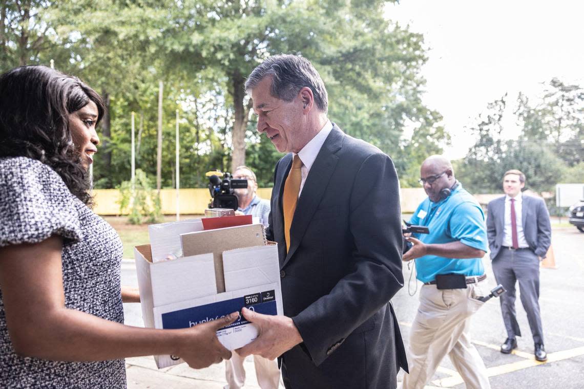 Gov. Roy Cooper, right, hands a box of supplies to Principal Kimberly Vaught at Allenbrook Elementary School in Charlotte, N.C., on Monday, September 12, 2022.