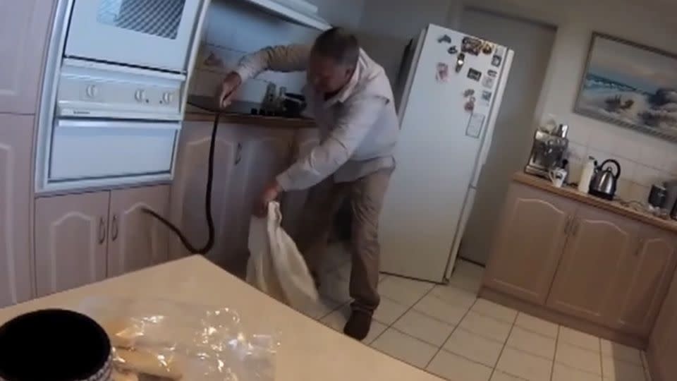 A woman can be heard shrieking in the background as Mr Burrell safely removes the snake from her kitchen. Photo: Facebook