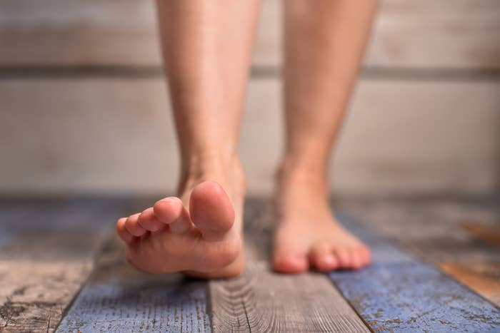 Close-up of a person's bare feet stepping forward on a wooden floor