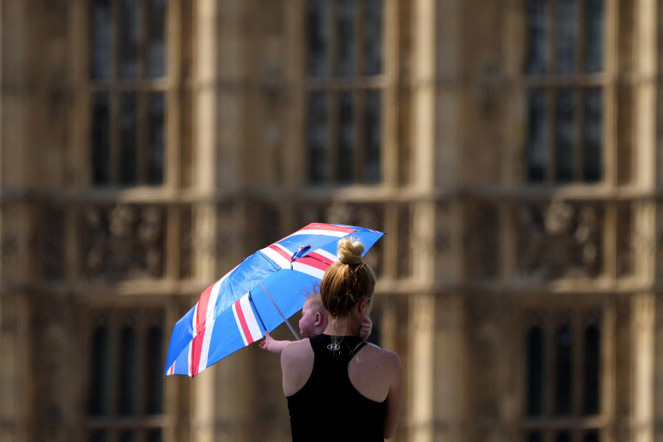 Una madre protege a su bebé del sol con un paraguas el martes 19 de julio de 2022, mientras camina por el puente de Westminster en Londres. (AP Foto/Frank Augstein)