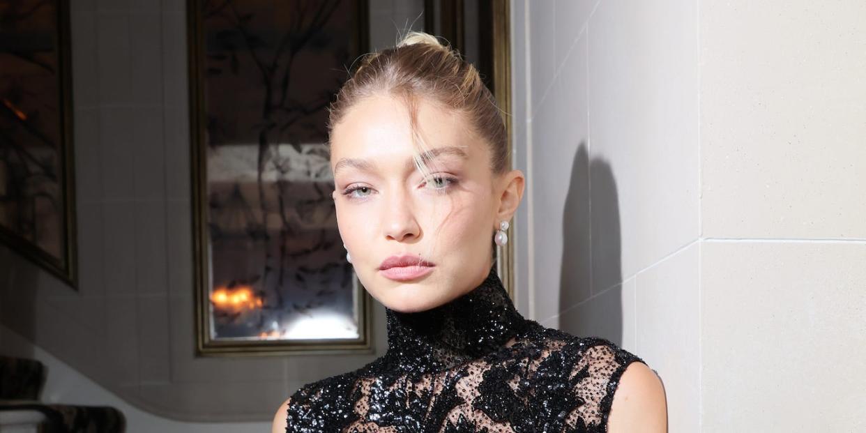 Gigi Hadid leans against a wall in a short black lace and sequin dress at the Miu Miu dinner for Paris Fashion week on October 3, 2023
