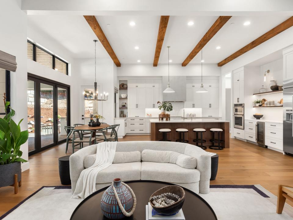 An open-concept living room with kitchen in background with white furniture and wooden details in both rooms