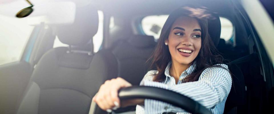 Happy woman driving a car and smiling. Cute young success happy brunette woman is driving a car. Portrait of happy female driver steering car with safety belt