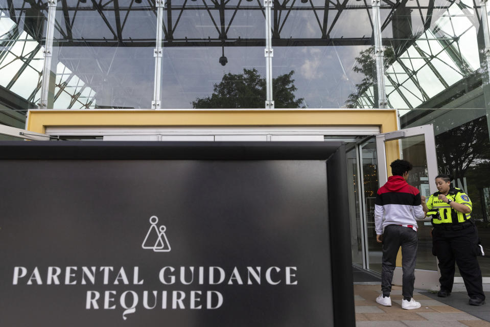 A security guard places a wristband on a person outside the Mall in Columbia, Friday, May 12, 2023, in Columbia, Md. The mall has implemented a "Parental Guidance Required" program, which requires that all visitors under 18 be accompanied by an adult who is at least 21-years-old after 4 p.m. on Fridays and Saturdays. Those over 18 are offered an optional wristband to avoid being approached by a security guard inside the mall. (AP Photo/Julia Nikhinson)