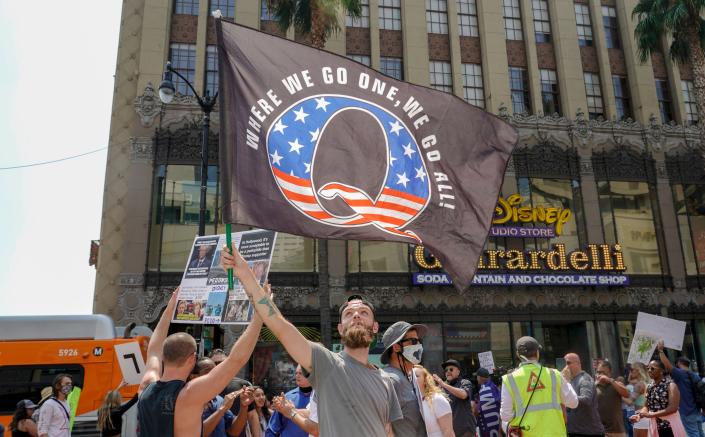 Manifestantes de QAnon, incluido uno que sostiene una pancarta que dice Donde vamos uno, vamos todos, durante una manifestación en una calle de la ciudad.