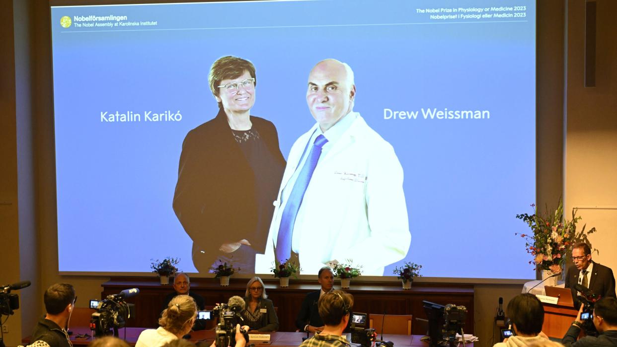  Thomas Perlmann, secretary of the Nobel committee, stands next to a large projector screen displaying the names and photos of Katalin Karikó and Drew Weissman. 