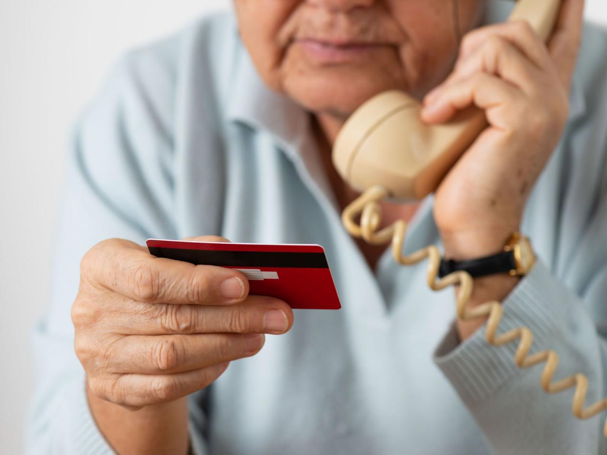 Senior woman using phone while holding credit card.