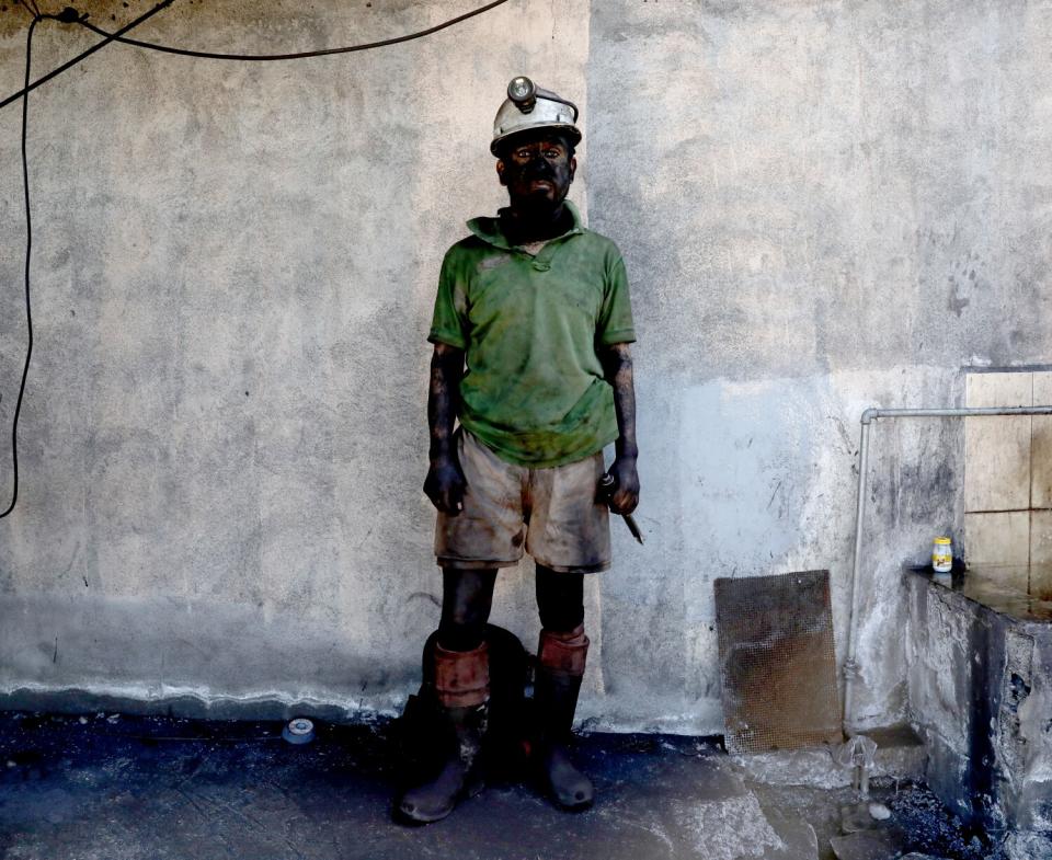 A man covered in coal dust and soot stands for a portrait.