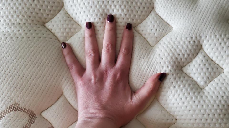 Our reviewer places her hand on the cover of the Saatva RX mattress to feel how cool it sleeps