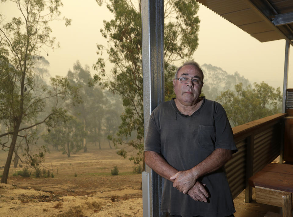 In this Jan, 11, 2020, photo, Joe Elvaro stands on the back deck his house at Burragate, Australia a day after an anticipated wildfire impact failed to come. It seemed imminent to those hunkering at the fire station that "The Beast" would finally roar through. But on this night the wildfire only crept closer, prodding forward a few tentative fingers before going dormant again as the winds died. (AP Photo/Rick Rycroft)