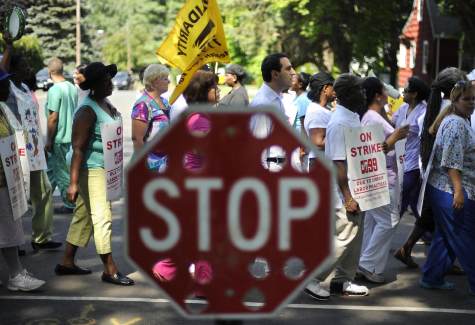 Nursing home workers march behind a stop sign at the entrance to Newington Health Care Center in Newington, Conn., Wednesday, July 11, 2012. Workers at five HealthBridge-owned nursing homes around the state went on strike last week after the health care company declined to return to the bargaining table. (AP Photo/Jessica Hill)