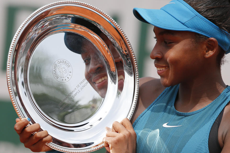 FILE - In this June 9, 2018, file photo, Cori Gauff is reflected in her trophy after defeating Caty McNally in the girls' singles final match of the French Open tennis tournament in Paris. Venus and Serena Williams remain a nearly constant presence at the U.S. Open since the debut of Arthur Ashe Stadium 21 years ago. Their 30 combined Grand Slam singles titles have left a mark on aspiring young players and the tennis landscape. Gauff, the No. 1 junior, once practiced on the same park courts in Delray Beach, Florida, as the Williams sisters. (AP Photo/Thibault Camus, File)