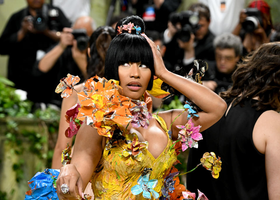 Nicki Minaj at a red carpet event, wearing a bold floral-themed dress with intricate flower details, surrounded by photographers