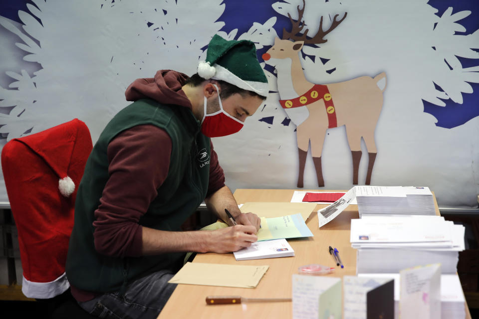 A postal worker who call themselves "Elves" open envelopes addressed to "Pere Noel" - Father Christmas in French - decorated with love hearts, stickers and glitter, in Libourne, southwest France, Monday, Nov. 23, 2020. Letters pouring by the tens of thousands into Santa's mailbox offer a glimpse into the worries and hopes of children awaiting a pandemic-hit Christmas. Along with usual pleas for toys and gadgets, kids are also mailing requests for vaccines, for visits from grandparents, for life to return to the way it was. The office estimates that one letter in three mentions the pandemic. (AP Photo/Francois Mori)