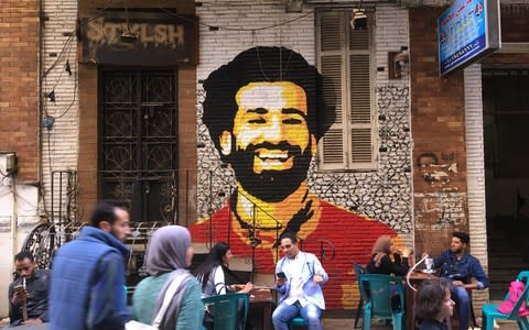 A picture taken on April 4, 2018 shows people sitting at a cafe in downtown Cairo with a mural depicting Liverpool FC's Egyptian striker Mohamed Salah painted in the background - Credit: AFP/Getty Images