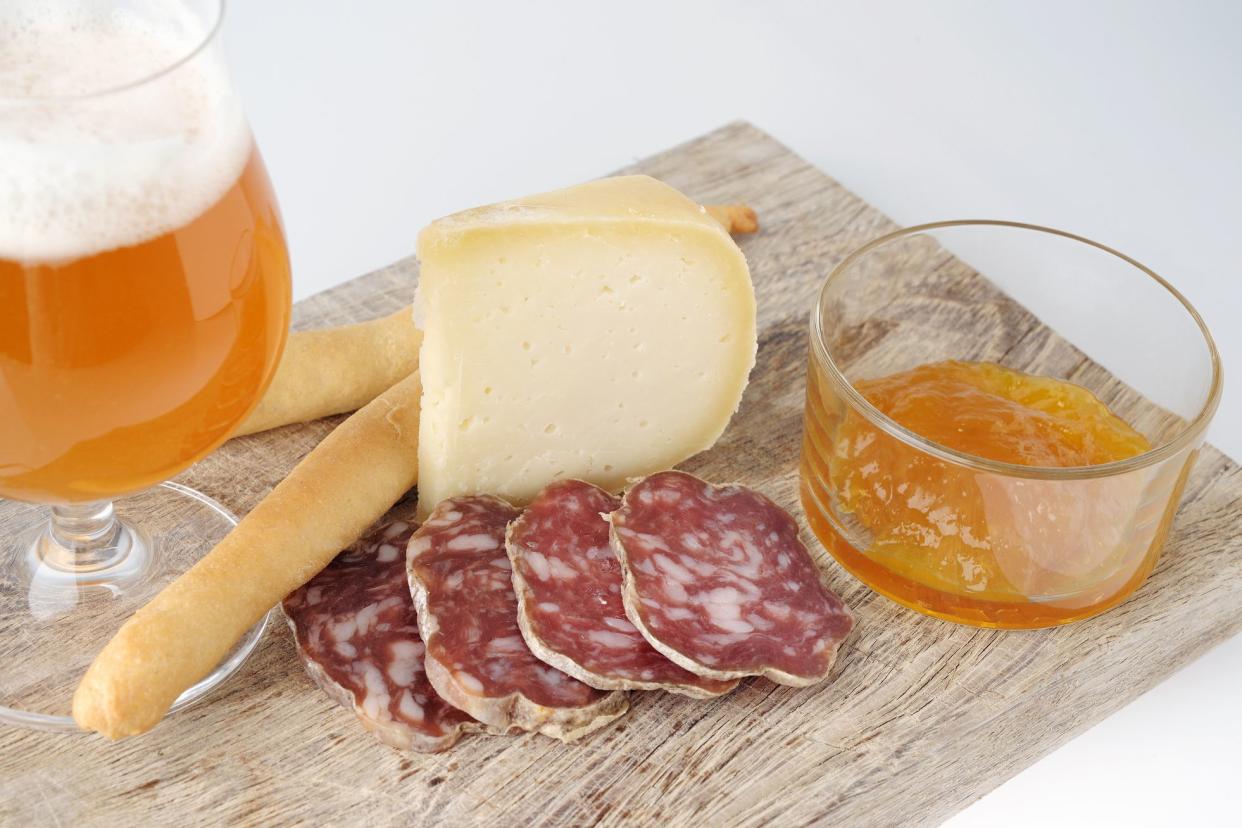 jam, glass of beer, sausage, and cheese on wooden cutting board