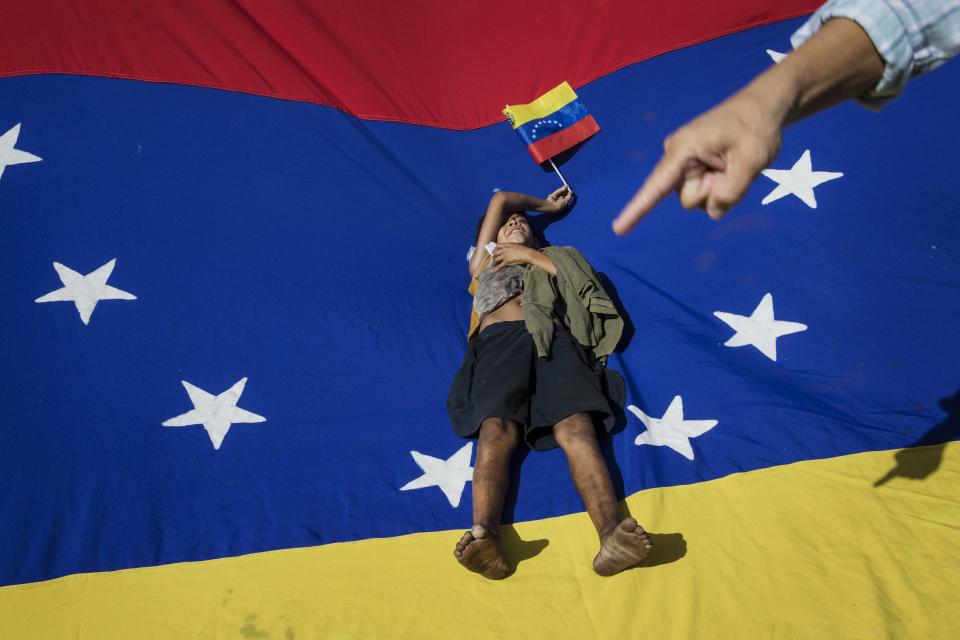 A man points at Oliver Duque, a homeless boy resting on top of a Venezuelan national flag during a demonstration called by opposition politician Juan Guaido, who's urging masses into the streets to force President Nicolás Maduro from power, in Maracaibo, Venezuela, Saturday, Nov. 16, 2019. Guaido called nationwide demonstrations to re-ignite a campaign against Maduro launched in January that has lost steam in recent months. (AP Photo/Rodrigo Abd)