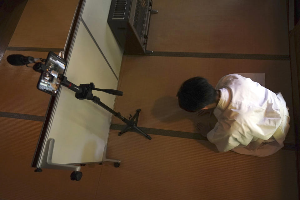 In this May 8, 2020, photo, a priest prays while checking the device for a livestream prayer during a 10-day trial of "online shrine" visit program at Onoterusaki Shrine in downtown Tokyo, allowing its visitors to join rituals from their homes. The shrine also accepted from worshipers their prayer messages, which were printed on a virtual wooden tablet each and offered to the Shinto gods to keep away evil spirits and the epidemic. (AP Photo/Eugene Hoshiko)