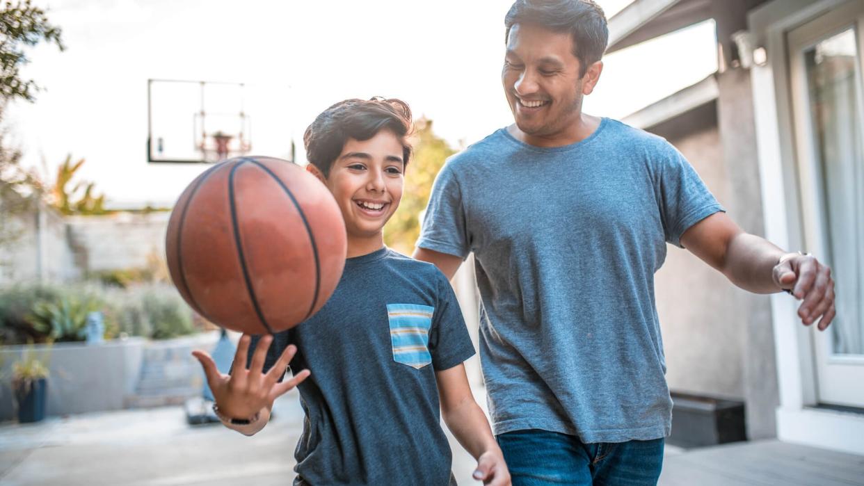 Happy boy spinning basketball while walking by father.