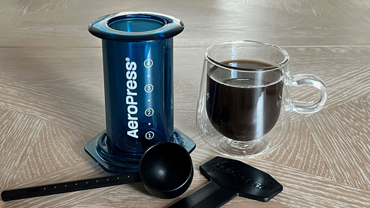  AeroPress Clear Color coffee press in blue with accessories and coffee mug. 