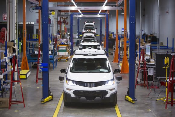 A line of white Chevrolet Bolt EVs with visible self-driving sensor hardware awaiting final assembly at GM's Orion Assembly Plant in Orion Township, Michigan.