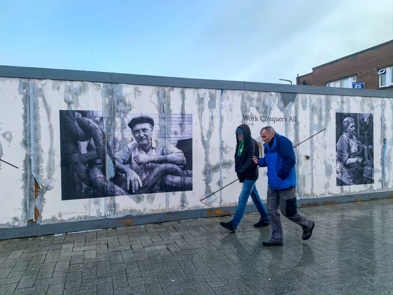 Men walk past damaged photograph of industrial worker in West Bromwich