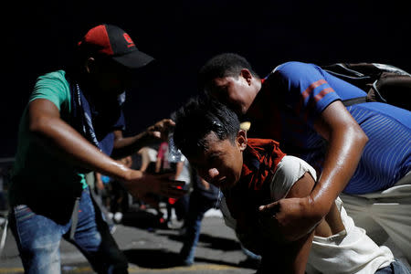 A man, part of a caravan of thousands of migrants from Central America en route to the U.S, washes his face from gas during a clash with the Mexican Police after they pull down the border gate with the intention to carry on their journey, in Tecun Uman, Guatemala, October 28, 2018. REUTERS/Carlos Garcia Rawlins