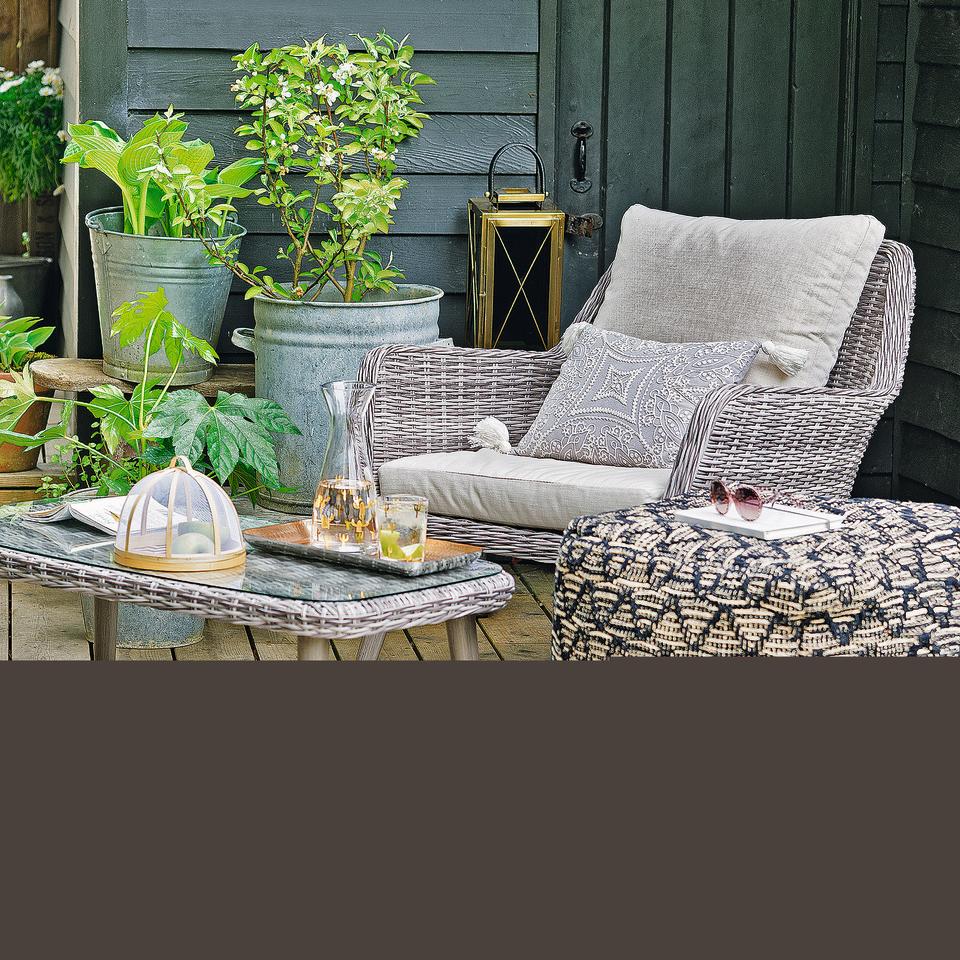 Garden with set of beige rattan furniture with glass top on table.