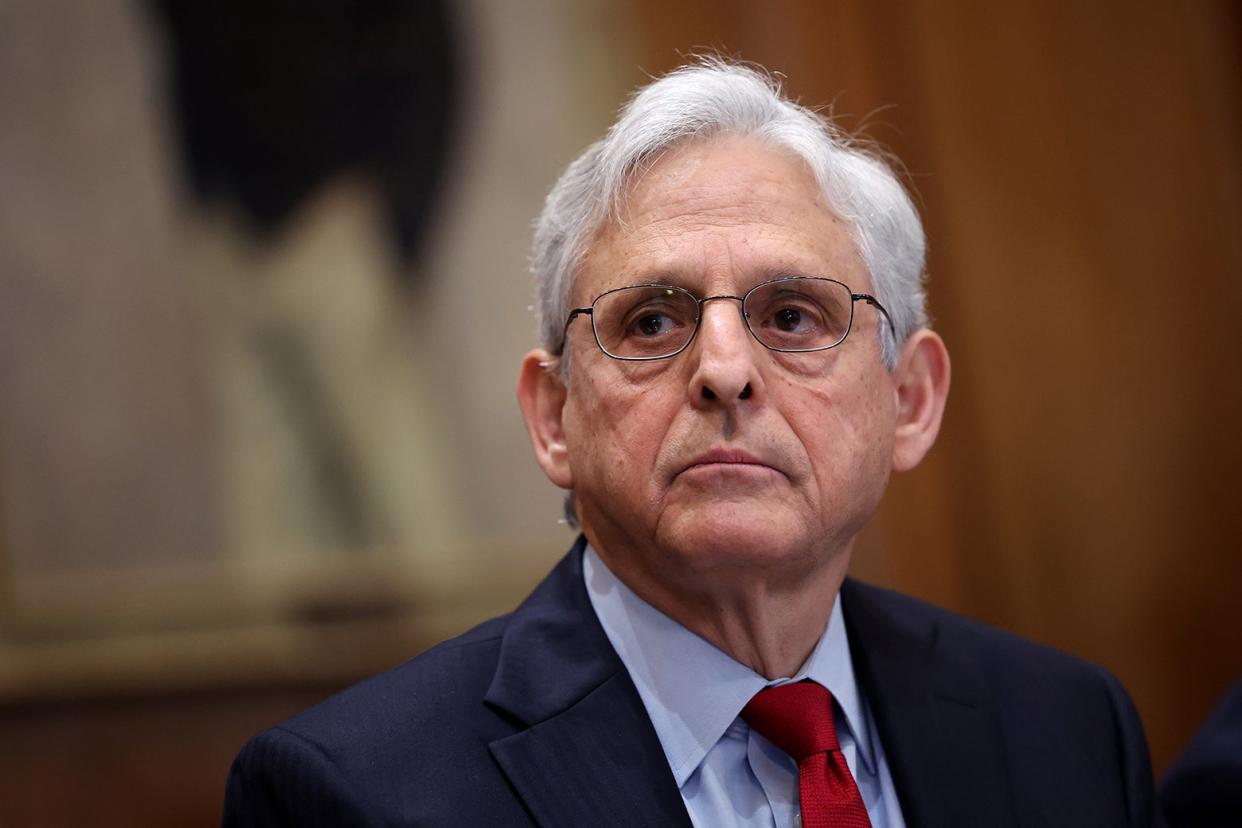 Garland looks straight ahead, wears glasses and a red tie.