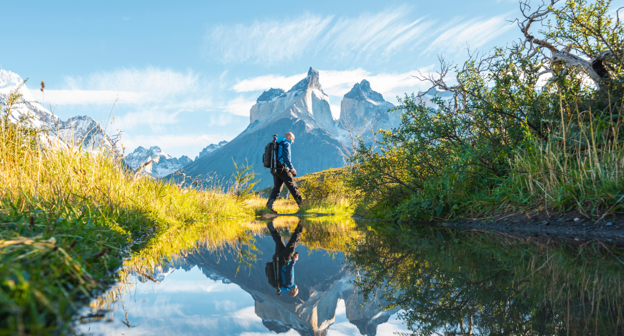 man hiking outside near mountains, mountain reflection in water, trees, man wearing hiking boots outside on trail hike