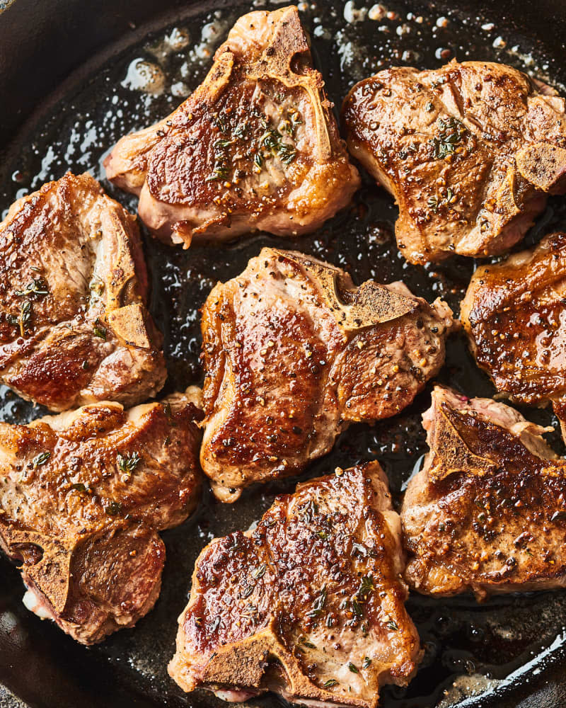 Browned lamb chops cooking in a cast iron pan.