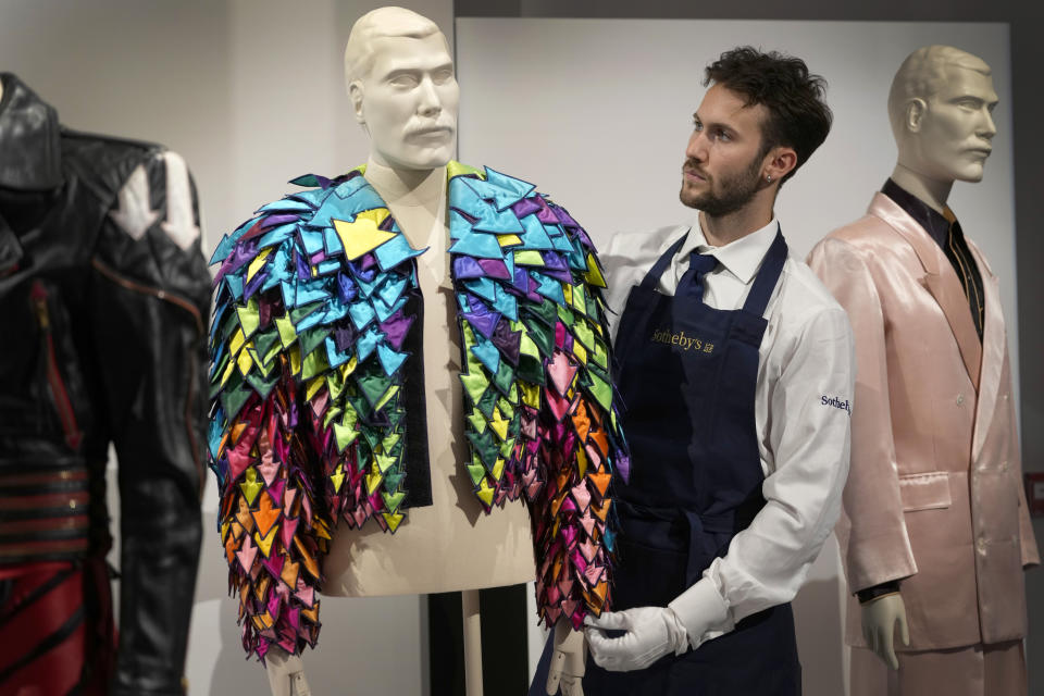 A Sotheby's handler displays a 'Rainbow Coloured Satin Arrow Applique Jacket from 1982' at Sotheby's auction rooms in London, Thursday, Aug. 3, 2023. More than 1,000 of Freddie Mercury's personal items, including his flamboyant stage costumes, handwritten drafts of “Bohemian Rhapsody” and the baby grand piano he used to compose Queen's greatest hits, are going on show in an exhibition at Sotheby's London ahead of their sale. (AP Photo/Kirsty Wigglesworth)