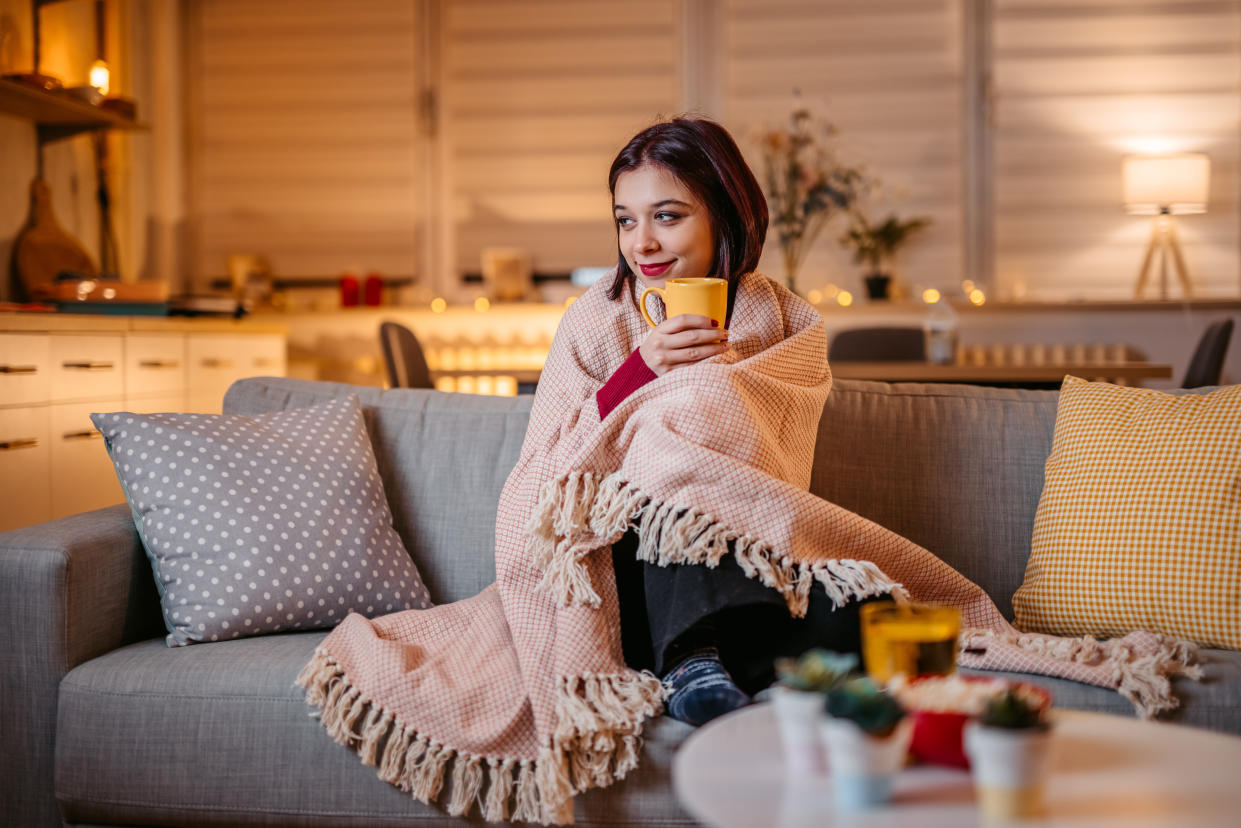 Beautiful young woman drinking hot tea wrapped in blanket on sofa at home. winter blues