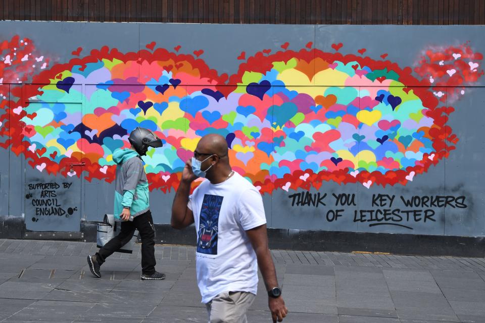 A man wearing a face mask as a precaution against the transmission of the novel coronavirus and a devliery worker walk past a piece of street art thanking key workers for their efforts during the pandemic in the centre of Leicester, central England on July 17, 2020, as local lockdown restrictions remain in force due to a spike in cases of the novel coronavirus in the city. - Boris Johnson said on July 17 he hoped Britain would "return to normality" by November despite being badly affected by the coronavirus and predictions of a second wave of cases during winter months. The prime minister announced fresh powers for councils to impose  local lockdowns, such as one currently in place in the English midlands city of Leicester, if there were increased number of cases elsewhere. The government on July 16 annouced a partially ease a two-week-old local lockdown in Leicester, after the number of new coronavirus cases had fallen, but remained well above the average for England which means restrictions on schools, early years childcare and non-essential retail stores will be relaxed from July 24, but that other measures impacting travel, social gatherings and the hospitality sector would remain. (Photo by DANIEL LEAL-OLIVAS / AFP) (Photo by DANIEL LEAL-OLIVAS/AFP via Getty Images)