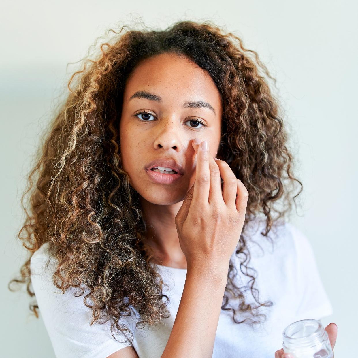  woman with eczema on her face applying cream 