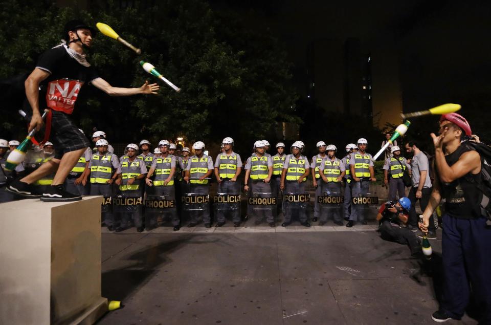 Demonstrators and jugglers perform in front of military policemen during a protest against the 2014 World Cup, in Sao Paulo March 13, 2014. An estimated 1,500 protesters gathered to march the streets of downtown Sao Paulo to show they are against the World Cup and against the costs associated with Brazil's hosting the sporting event. Activists are demanding more money be spent on education, health care, public transportation and to fight crime. REUTERS/Nacho Doce (BRAZIL - Tags: SPORT SOCCER WORLD CUP POLITICS CIVIL UNREST CRIME LAW)