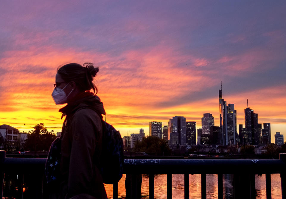 A woman wearing a face mask walks over a bridge with the buildings of the banking district in background in Frankfurt, Germany, Monday, Oct. 26, 2020. (AP Photo/Michael Probst)