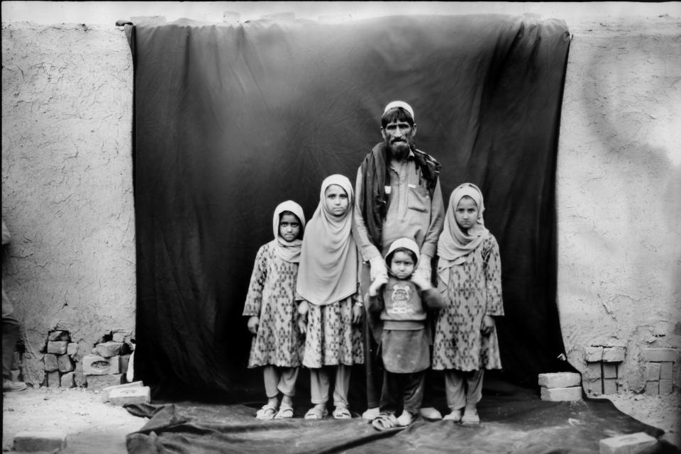 Khayesta Gul, 57, stands for a portrait with his children, from left, Osna, 5; Yesna, 8; Ali, 3, and Gulalai, 7, while taking a break from working in a brick factory on the outskirts of Kabul, Afghanistan, Tuesday, May 30, 2023. Khayesta, a seasonal brick worker, comes in the summer with thousands of other villagers to work in the brick factories and then goes back to Nangarhar where he lives the rest of the year. (AP Photo/Rodrigo Abd)