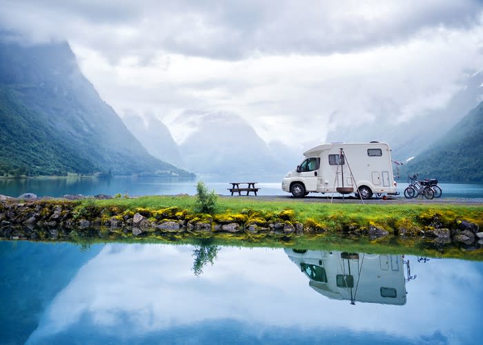 A camper parked in front of a mountain holiday scene.