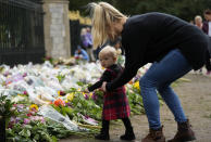 A woman helps a small girl to lay down a flower outside the gates of Windsor Castle in Windsor, England, Friday, Sept. 9, 2022. (AP Photo/Frank Augstein)