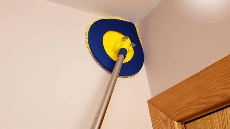 the yellow and blue, teardrop-shaped wall mop being used to clean the upper corner of a room